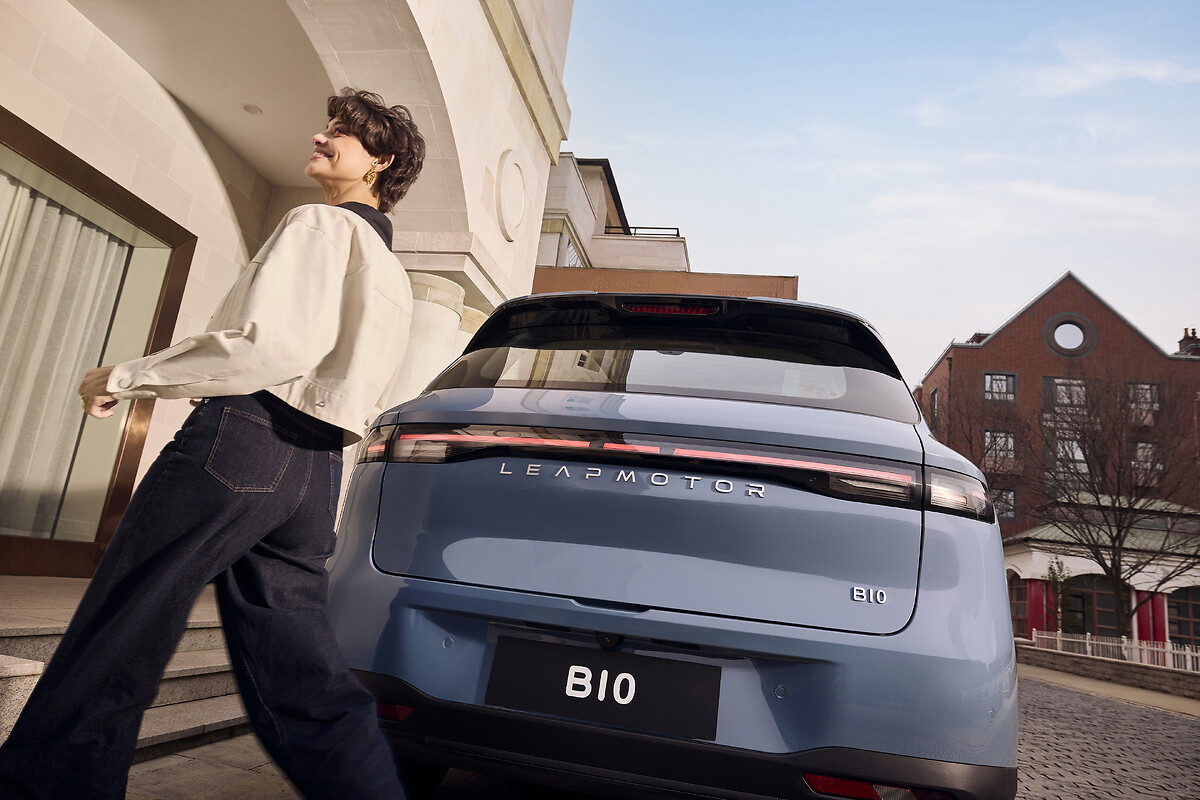 Woman leaning against light blue Leapmotor B10 rear quarter panel showing full-width LED tail lights