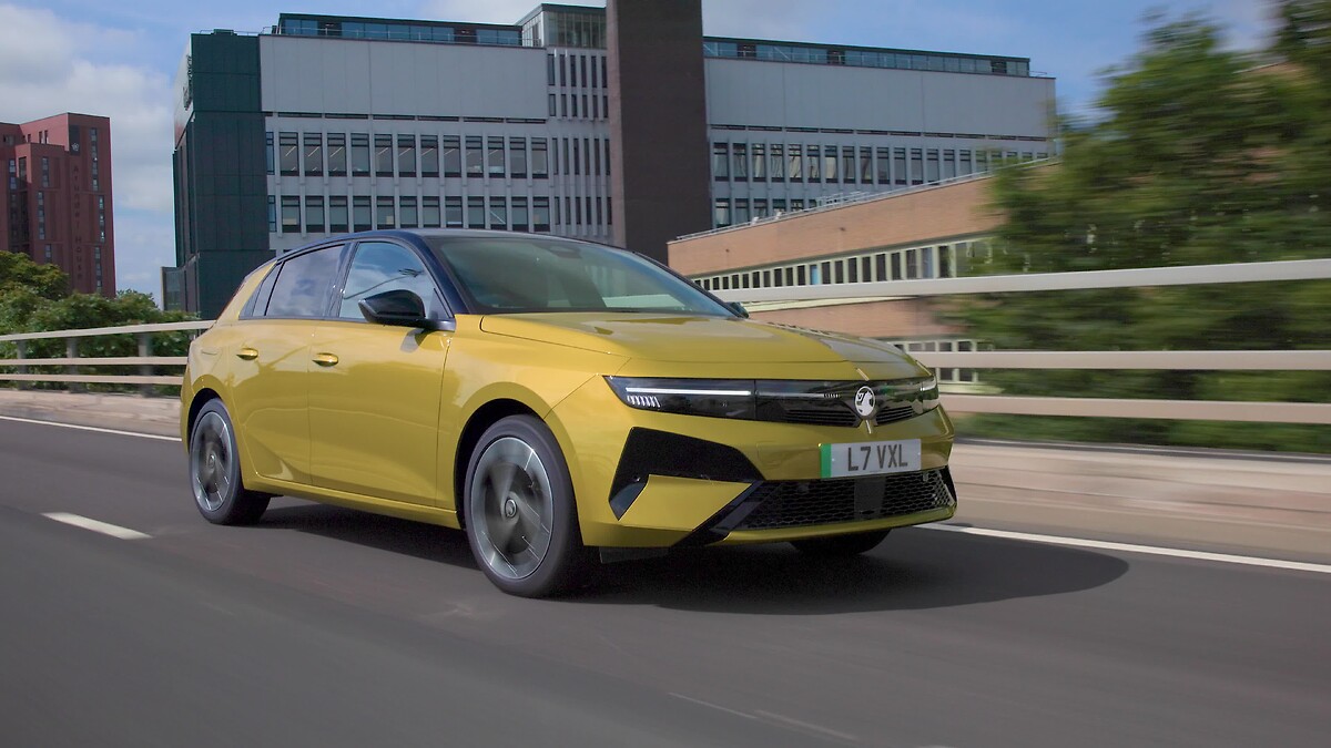Yellow Vauxhall Astra driving on highway with urban buildings